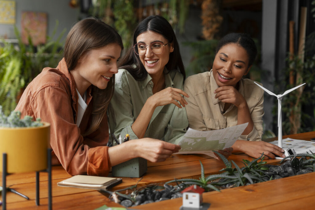 Três mulheres analisando projetos ambientais e sorrindo em um ambiente de trabalho colaborativo, representando carreiras sustentáveis em crescimento