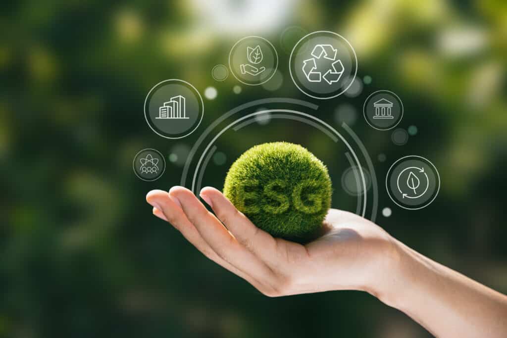 Mão segurando esfera verde com o termo ESG, cercada por ícones de sustentabilidade, representando a aplicação dos critérios ESG na eficiência produtiva.