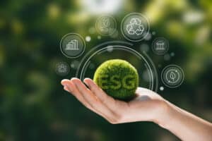 Mão segurando esfera verde com o termo ESG, cercada por ícones de sustentabilidade, representando a aplicação dos critérios ESG na eficiência produtiva.