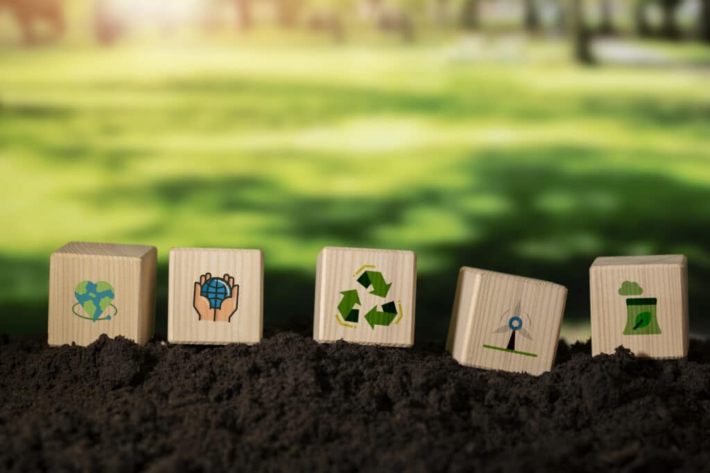Blocos de madeira com ícones de reciclagem, energia renovável e preservação ambiental simbolizando o debate sobre consumo consciente vs. green consumerism.